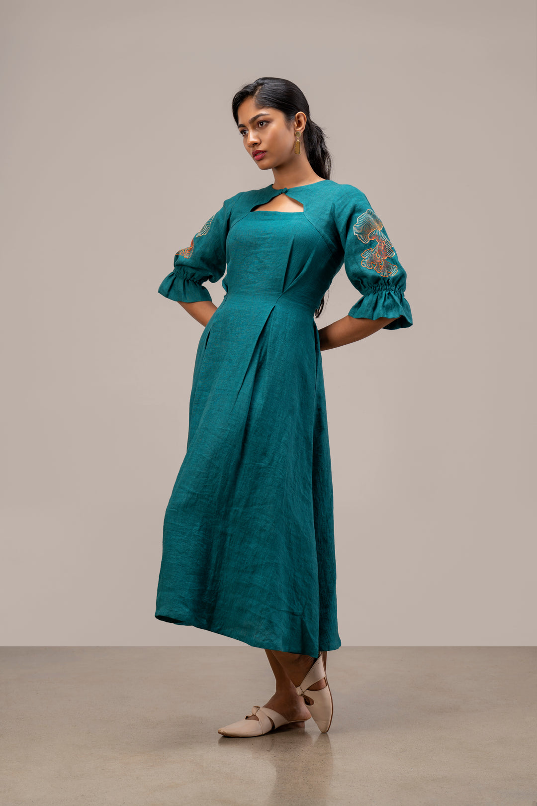 Woman wearing a teal dress with floral sleeves against a neutral background